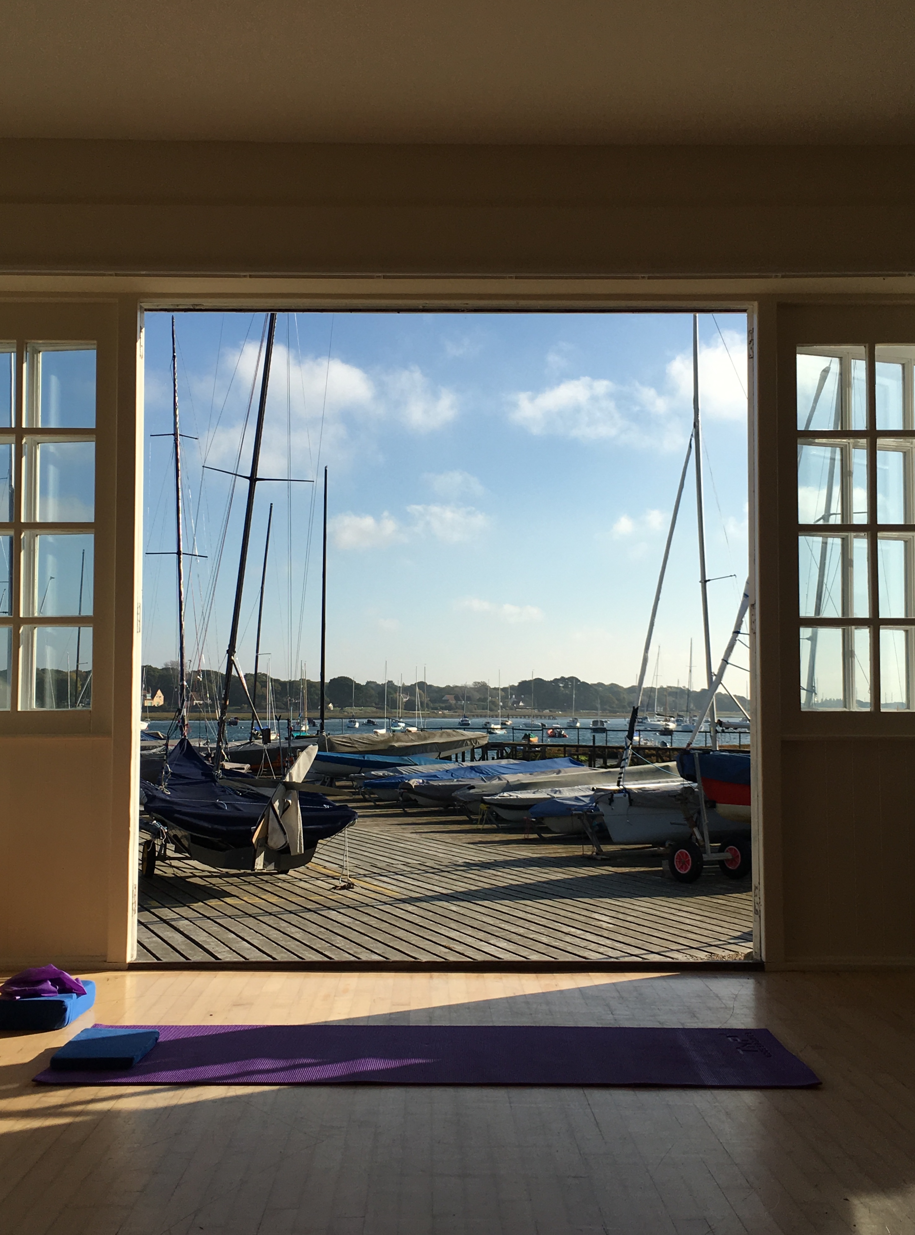 The class room at Chichester Yacht Club: a purple exercise mat unrolled on a wooden floor, with open doors onto the marina — dinghies, masts and water beyond.